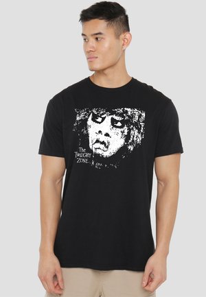 Schwarzes Baumwoll-T-Shirt mit einem weißen Grafikdruck eines Gesichts und dem Text "The Twilight Zone." Kurze Ärmel, Rundhalsausschnitt.