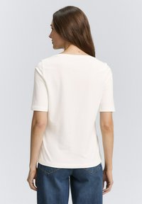 Witte kortemouwtop met een ronde hals, gladde textuur, losse pasvorm, gecombineerd met donkerblauwe wijde jeans, gezien van achteren.