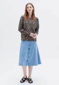 Leopardmönstrad långärmad topp, kombinerad med en ljusblå denimkjol med knappstängning fram och svarta sandaler.