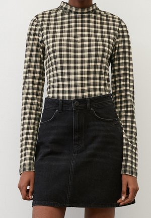 Kobieta ubrana w długi rękaw, czarno-białą kratowaną bluzkę, wpuszczoną w wysokodołkową czarną dżinsową spódnicę z przednimi kieszeniami.