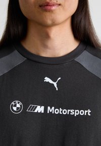 Sort bomulds t-shirt med grå skulderdetaljer, og hvide logoer for Puma og BMW Motorsport trykt på forsiden.