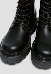 Czarne skórzane buty z połyskiem, okrągłym noskiem, grubymi, teksturowanymi podeszwami i kontrastującymi szarymi sznurówkami. Posiadają przeszycia wzdłuż krawędzi.