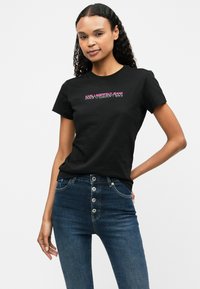 Melna kokvilnas t-kreklu ar izteiksmīgu krāsainu "Karl Lagerfeld Jeans" tekstu. Apvienots ar augstām ziliem džinsiem ar pogām.