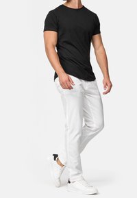 T-shirt noir à manches courtes en coton associé à un jean en denim blanc et des baskets blanches avec un accent noir sur le talon.