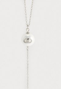 Collana in tonalità argento con un pendente sferico bianco dotato di un logo ritagliato, sospeso da una catena collegata.
