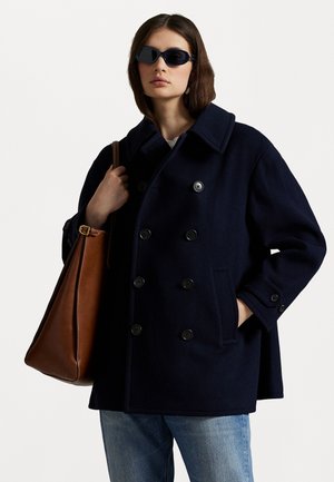 Navy wool peacoat with double-breasted buttons, large collar, side pockets, paired with a brown leather bag and dark sunglasses.