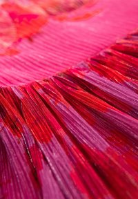 Franje stof in verschillende tinten roze en rood, met een glanzende textuur en gelaagd ontwerp dat diepte en beweging creëert.