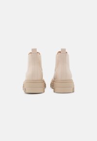 Beżowe botki za kostkę z gładką skórzaną powierzchnią, elastycznymi panelami bocznymi oraz grubą gumową podeszwą, z pętelkami ułatwiającymi zakładanie.