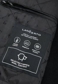 Czarny pikowany materiał z metką zawierającą instrukcje pielęgnacji. Tekst podkreśla komfort termiczny, wiatroszczelność oraz szczegóły dotyczące zawartości wełny.