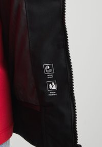 Black windproof and water-repellent jacket interior displayed, featuring care labels with icons for windproof and water-repellent properties.