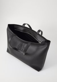 Černá kožená taška přes rameno s vyraženým logem "CK", otevřený vršek, dvojité uši a zipová vnitřní kapsa pro bezpečné uložení.