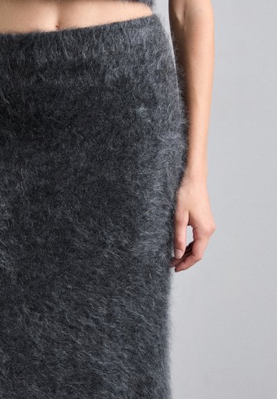 Grijze gefilte wol rok met een zachte, gestructureerde oppervlakte, een aansluitend ontwerp en een hoge tailleband, die net onder de knie reikt en vastgehouden wordt door een hand.