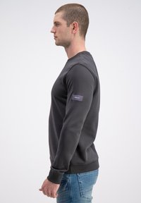 Ciemnoszara bluza z długimi rękawami i okrągłym dekoltem. Posiada boczną metkę na lewym rękawie oraz ściągacze na mankietach. Noszona z niebieskimi dżinsami.