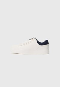 Fehér alacsony szárú sportcipő tengerészkék sarkammal, fehér fűzőkkel és arany "Tommy Hilfiger" logóval oldalán.