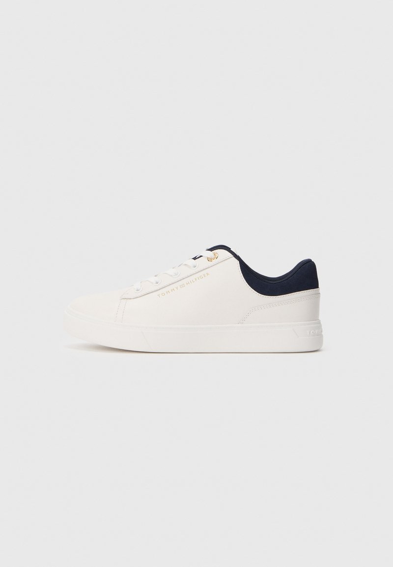 Fehér alacsony szárú sportcipő tengerészkék sarkammal, fehér fűzőkkel és arany "Tommy Hilfiger" logóval oldalán.