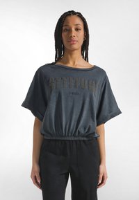 Top corto azul oscuro con mangas cortas anchas, con la inscripción "ACTITUD" en letras en relieve y una cintura elástica. Textura de tela lisa.