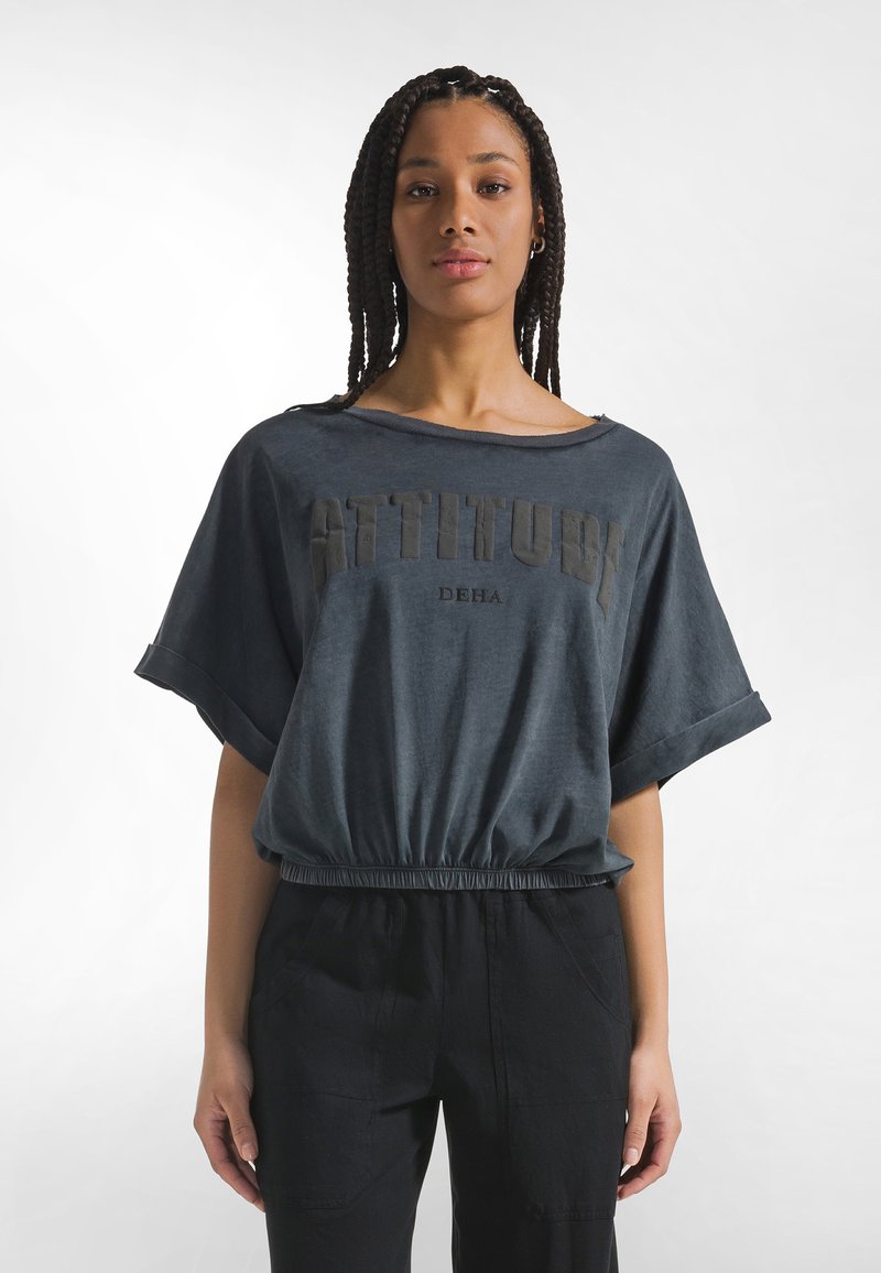 Top corto azul oscuro con mangas cortas anchas, con la inscripción "ACTITUD" en letras en relieve y una cintura elástica. Textura de tela lisa.