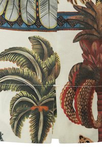 Close-up of fabric with printed tropical leaves and palm trees in green, brown, and red tones with a stitched seam in the center.
