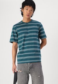 Camiseta de manga corta en color azul agua con rayas horizontales blancas. Confeccionada en tejido suave, presenta un cuello redondo y un corte relajado.