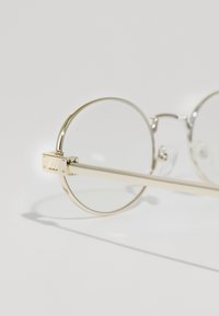 Ochelari rotunzi din metal cu un cadru subțire de aur, lentile transparente și un detaliu rectangular la balama. Temele sunt elegante și drepte.