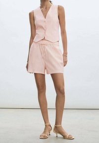 Jasnoróżowa kamizelka w pionowe paski, z zapięciem na guziki, w zestawie z pasującymi szortami. Materiał wydaje się lekki o gładkiej fakturze.