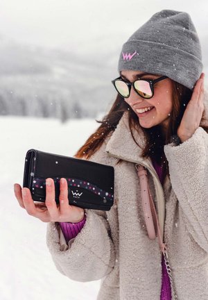 Black wallet with curved pink and purple dotted pattern, held by a person in a cozy beige sherpa jacket against a snowy background.