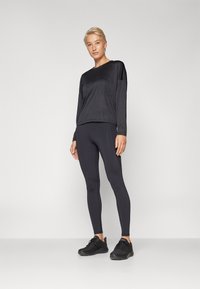 Musthave mustriline käe pikkus spordisärk, millel on lõdvestunud lõige, koos mustade retuuside ja mustade jooksujalatsitega. Sile tekstuur ja lihtne disain.