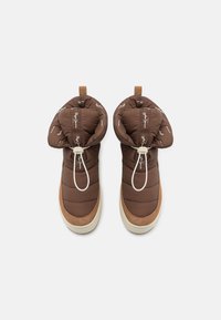 Zapatillas marrones con aislamiento, parte superior suave y texturizada, cordón ajustable y suela de goma color crema. Marca destacada en el cuello.