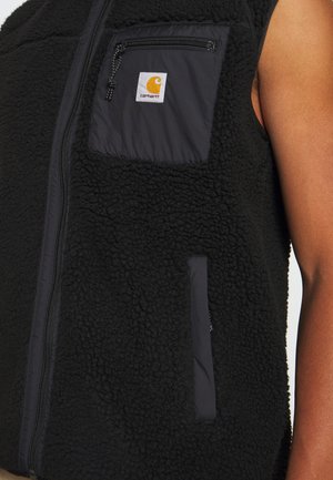 Schwarze Fleeceweste mit Frontreißverschluss, Reißverschlusstasche auf der Brust mit Carhartt-Logo-Patch, getragen über einem nackten Arm.