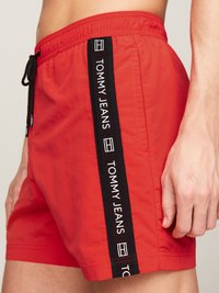 Shorts da bagno rossi realizzati in tessuto leggero, con una striscia laterale nera con il logo "TOMMY JEANS", vita elasticizzata e dettaglio con cordino.