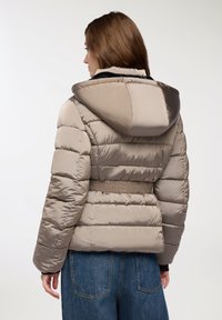 Giubbotto a vento in beige chiaro, design trapuntato, dotato di cappuccio, vita elasticizzata e interno nero a contrasto. Texture morbida, materiale resistente all'acqua.