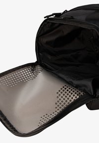 Μαύρη τσάντα με φερμουάρ. Το εσωτερικό διαθέτει λείο, ανοιχτό γκρι υλικό με διάτρητα σχέδια και συμπαγή μαύρη επένδυση.