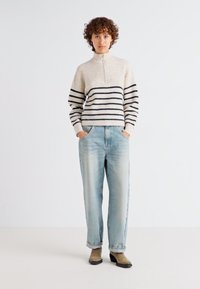 Light beige knit sweater with navy stripes, high collar, front zipper; paired with loose-fit light blue denim jeans and ankle boots.