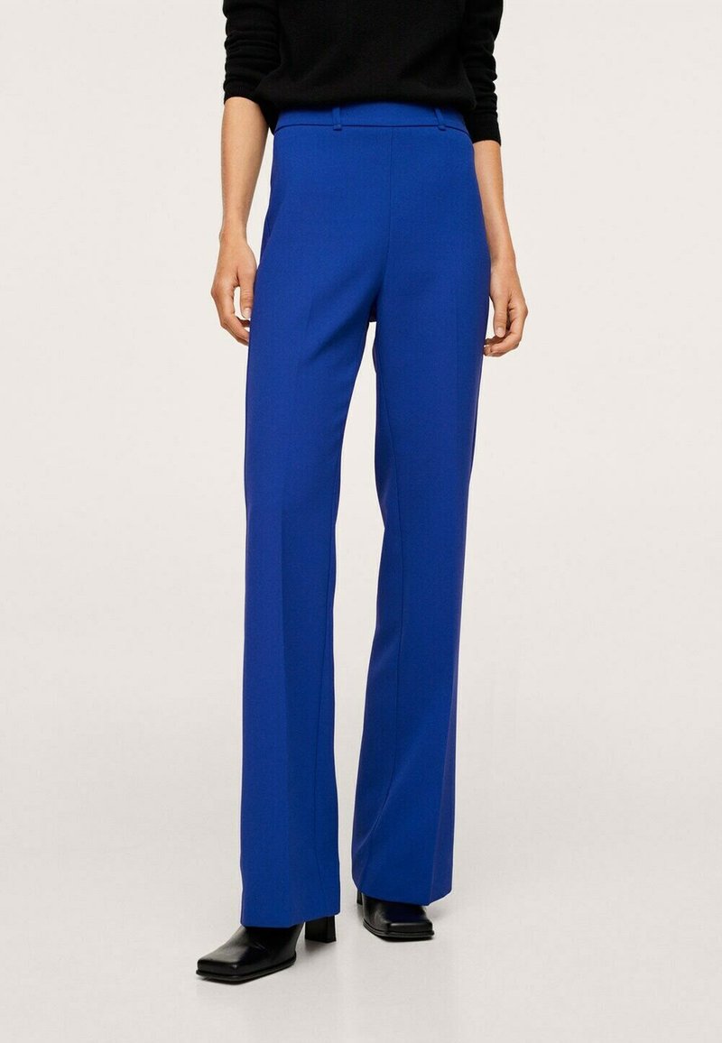 Pantalon bleu sur mesure avec une coupe droite, doté de poches latérales et d'un tissu lisse et structuré. Porté avec des chaussures noires.