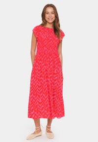 Robe maxi de couleur rose vif avec un motif abstrait contrastant. Elle présente des manches courtes à volants, un corsage smocké et une jupe fluide.