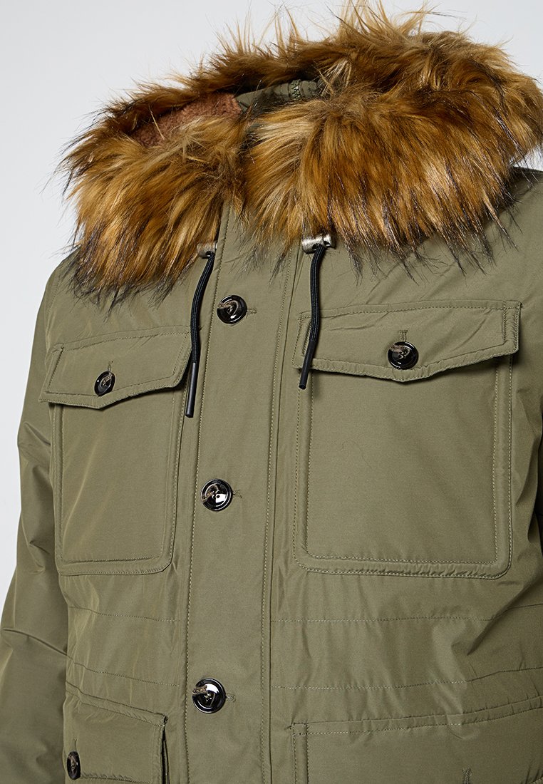 Oliwkowy parka z kapturem wyłożonym futrem, z czarnymi guzikami, zamykanymi kieszeniami i gładką fakturą, idealna na zimną pogodę.