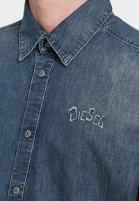 Μπλε τζιν πουκάμισο με γιακά κουμπωτό, μεταλλικά κουμπιά και κεντημένο λογότυπο "Diesel" σε ανοιχτ�ό μπλε στο στήθος. Ομαλή υφή.