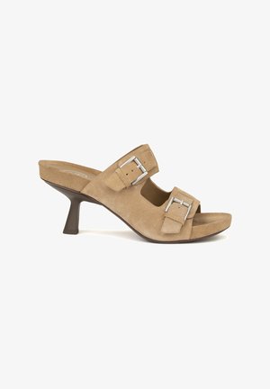 Mule in suede beige con punta aperta, dotata di due cinturini regolabili con fibbia e tacco affusolato di 7 cm. Superficie testurizzata, suola liscia, dettagli minimal.