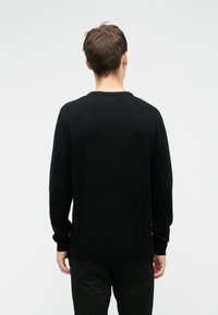 Schwarzer Strickpullover mit langen Ärmeln und einem gerippten Ausschnitt, ausgestattet mit einem geraden Saum und einem minimalistischen Design. Der Stoff wirkt weich und glatt.