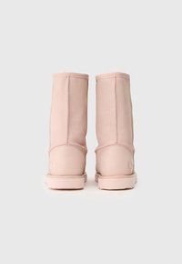 Pár mid-calf topánok svetloružovej farby s viditeľným šitím, plochými podrážkami a jemne embosovaným logom na päte, zobrazené zozadu.