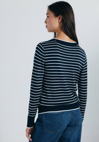 Marinblå och vit randig långärmad tröja med rund halsringning och ribbade mudd, tillsammans med blå jeans med hög midja.