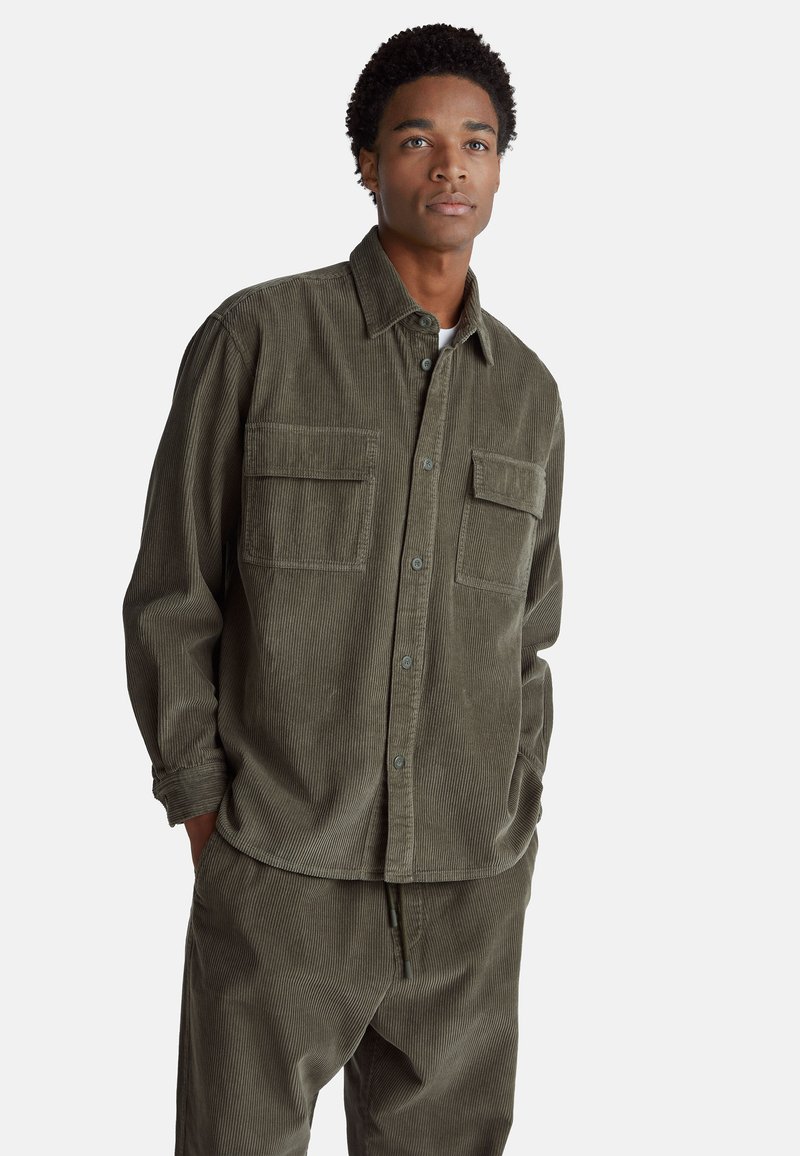 Camicia in corduroy verde oliva con due tasche sul petto, chiusura con bottoni e maniche lunghe, caratterizzata da un motivo a coste testurizzato.