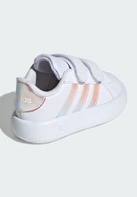 Zapatillas blancas con un upper sintético liso, que presentan tres franjas iridiscentes y correas de gancho y bucle. Suave collar acolchado en el tobillo.