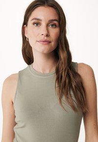 Débardeur côtelé vert clair avec un col haut, présentant une silhouette ajustée et une texture lisse. Design minimaliste sans motifs visibles.