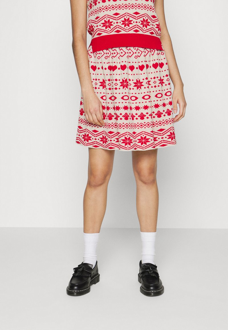 Vestido em padrão vermelho e branco com corpete justo e saia rodada, apresentando desenhos geométricos e florais. Sapatos pretos com franjas.