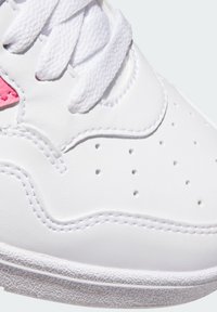 Tacco di una sneaker bianca con lacci bianchi testurizzati, fori di ventilazione perforati, doppia cucitura e un piccolo accento rosa vicino ai lacci.