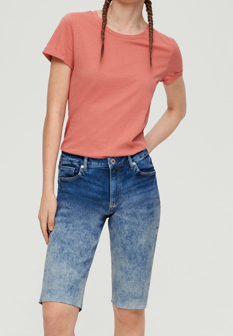 T-shirt en coton rose à manches courtes associé à un short bermuda en denim bleu avec un dégradé de couleur progressif et un ourlet effiloché.