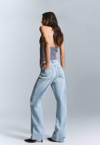 Light blue wide-leg jeans with a faded texture, featuring studded accents along the side and back pockets. Worn with a gray fitted top.