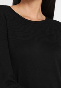 Maglione nero lavorato a maglia con scollo rotondo, strisce orizzontali testurizzate sul petto e maniche lunghe. Tessuto morbido con una silhouette aderente.