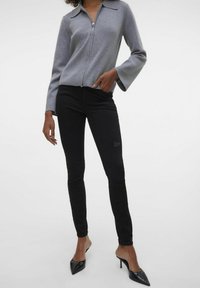 Šedý svetr na zip s límečkem, doplněný o černé skinny džíny s jemnou výšivkou. Černé lodičky s špičatou špičkou dotvářejí celý outfit.